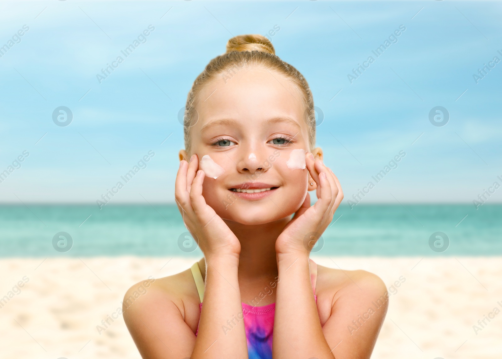 Image of Sun protection. Cute girl applying sunblock onto face on beach