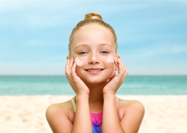 Image of Sun protection. Cute girl applying sunblock onto face on beach