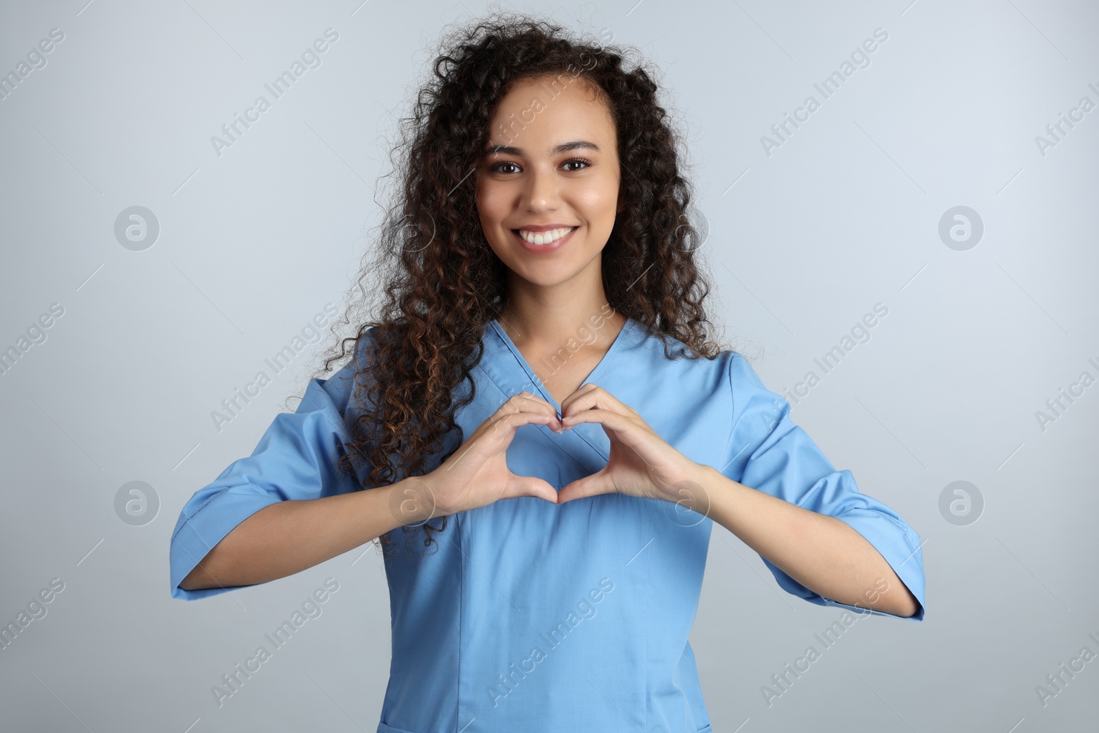 Photo of Happy young African-American doctor making heart with hands on light grey background