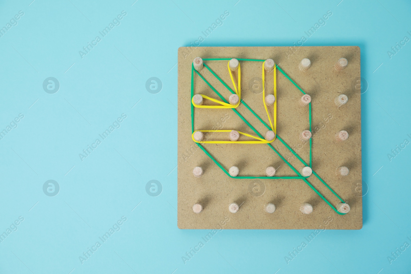 Photo of Wooden geoboard with leaf shape made of rubber bands on light blue background, top view and space for text. Educational toy for motor skills development