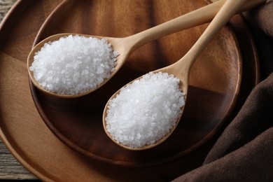 Photo of Organic salt in spoons on wooden table, closeup