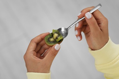 Photo of Woman eating kiwi with spoon on blurred background, closeup
