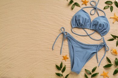 Stylish bikini, starfishes and leaves on sand, flat lay. Space for text