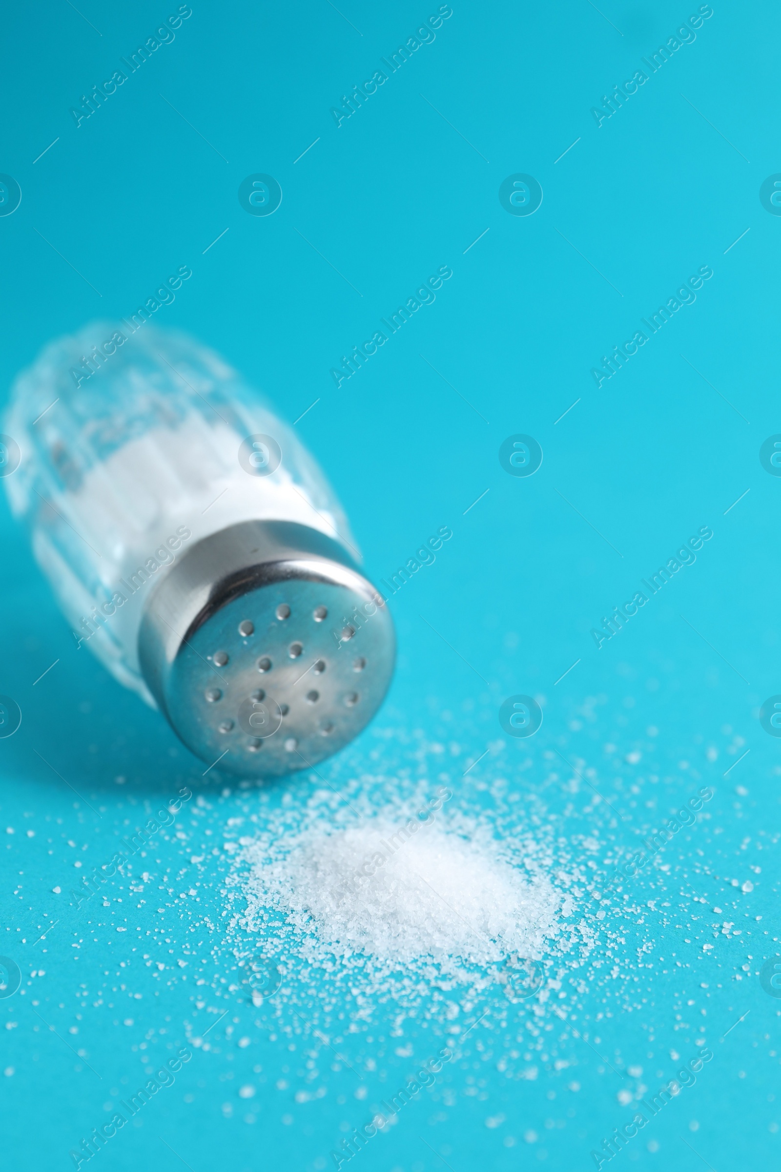 Photo of Organic white salt in glass shaker on light blue background, closeup. Space for text