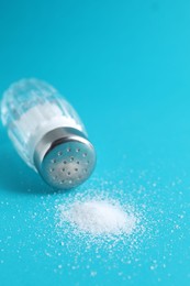 Photo of Organic white salt in glass shaker on light blue background, closeup. Space for text