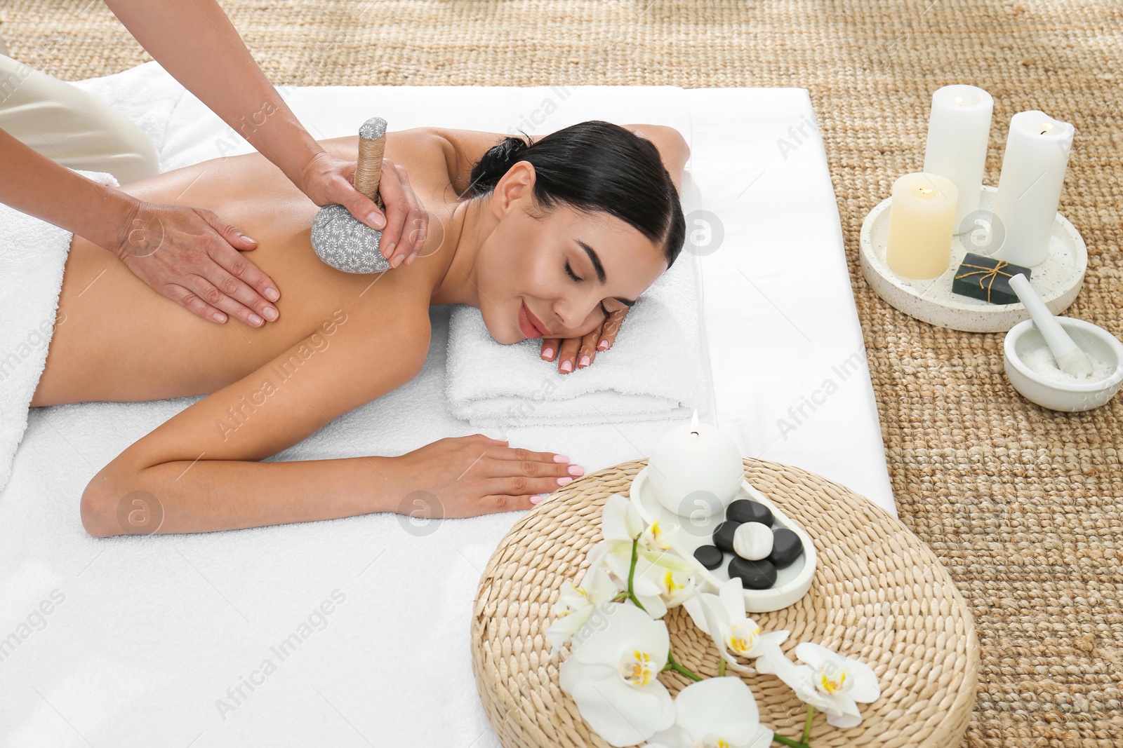 Photo of Young woman receiving herbal bag massage in spa salon