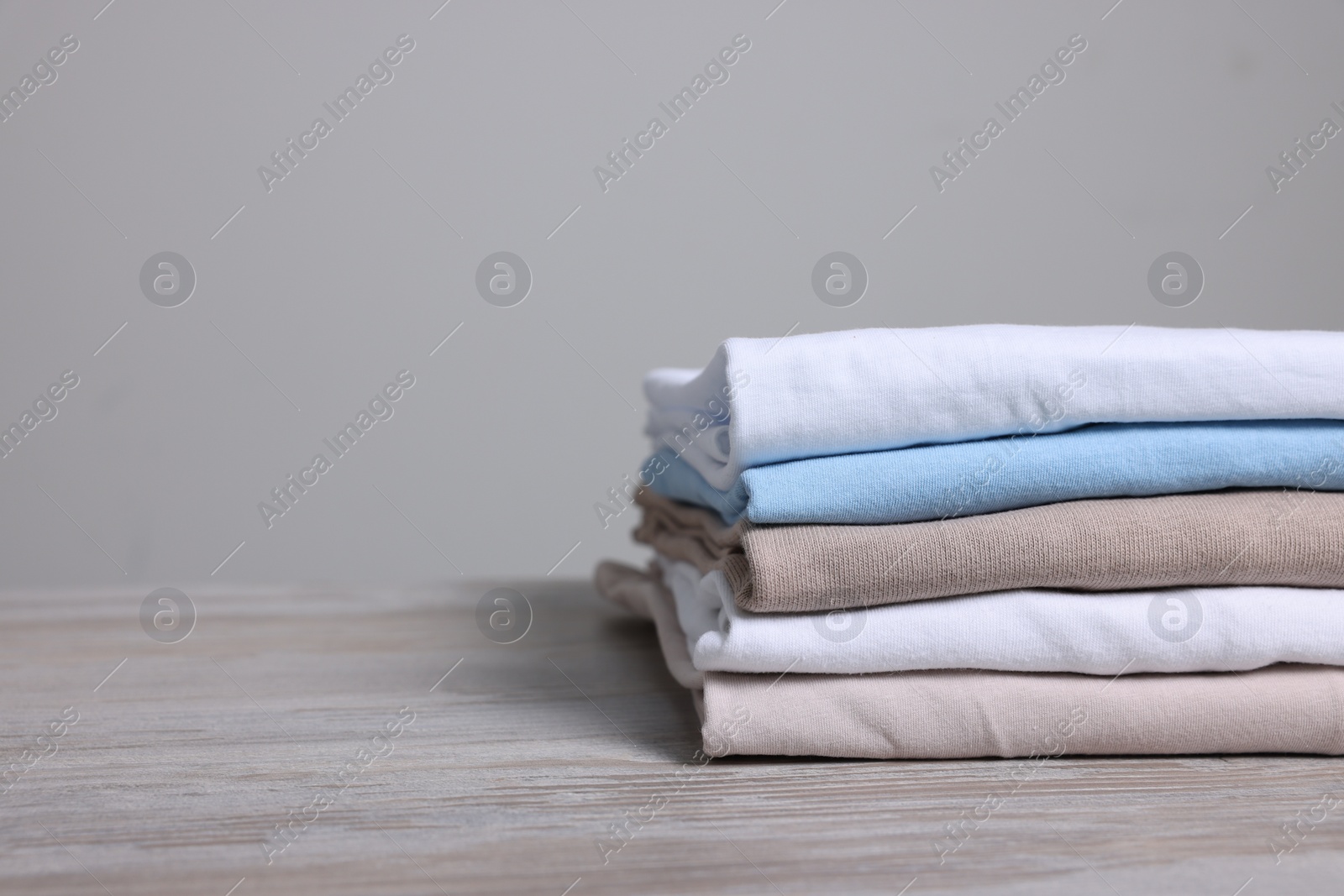 Photo of Sorting and organizing. Stack of different folded clothes on light wooden table, closeup. Space for text