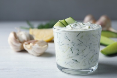 Photo of Glass bowl of Tzatziki cucumber sauce with ingredients on table, space for text