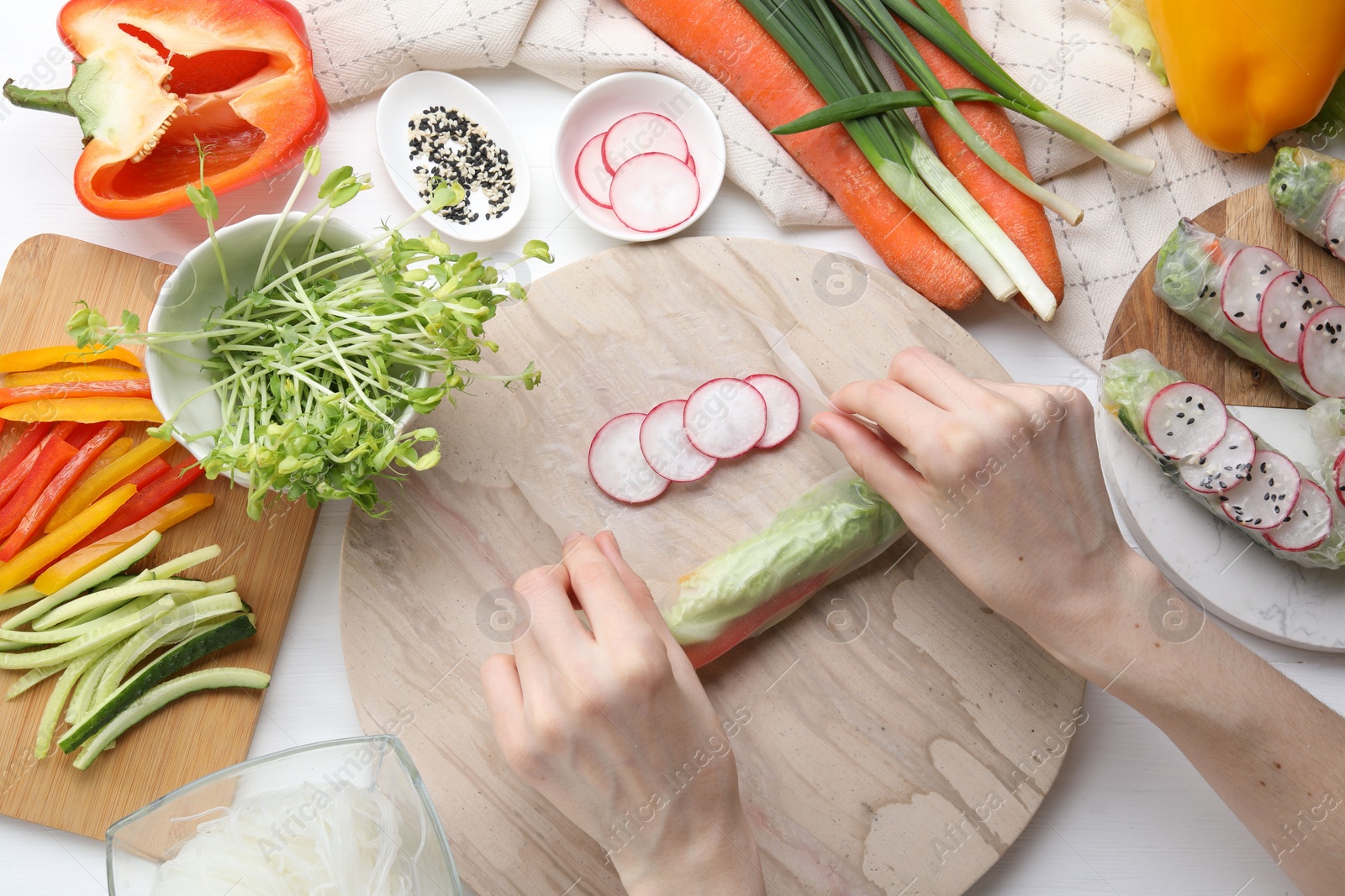 Photo of Woman wrapping spring roll at white wooden table with products, top view