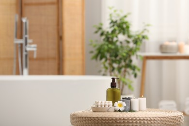 Photo of Spa products, burning candles and plumeria flower on wicker table in bathroom. Space for text