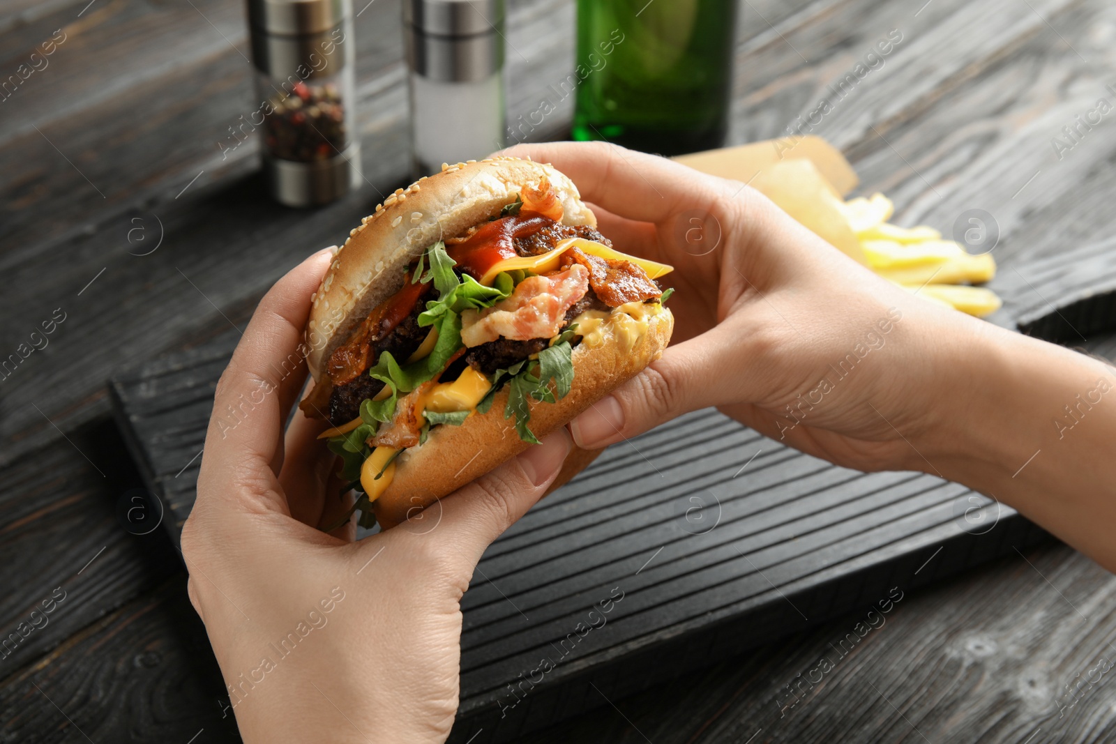 Photo of Woman holding tasty burger with bacon at table, closeup