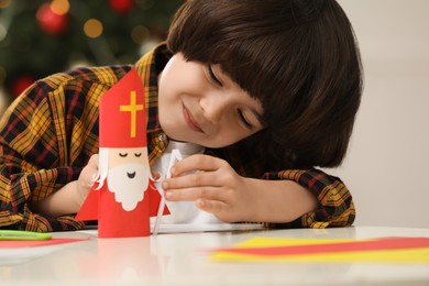 Photo of Cute little boy making paper Saint Nicholas toy at home