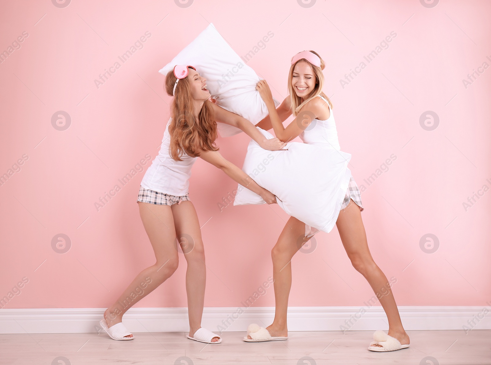 Photo of Two young women having pillow fight near color wall