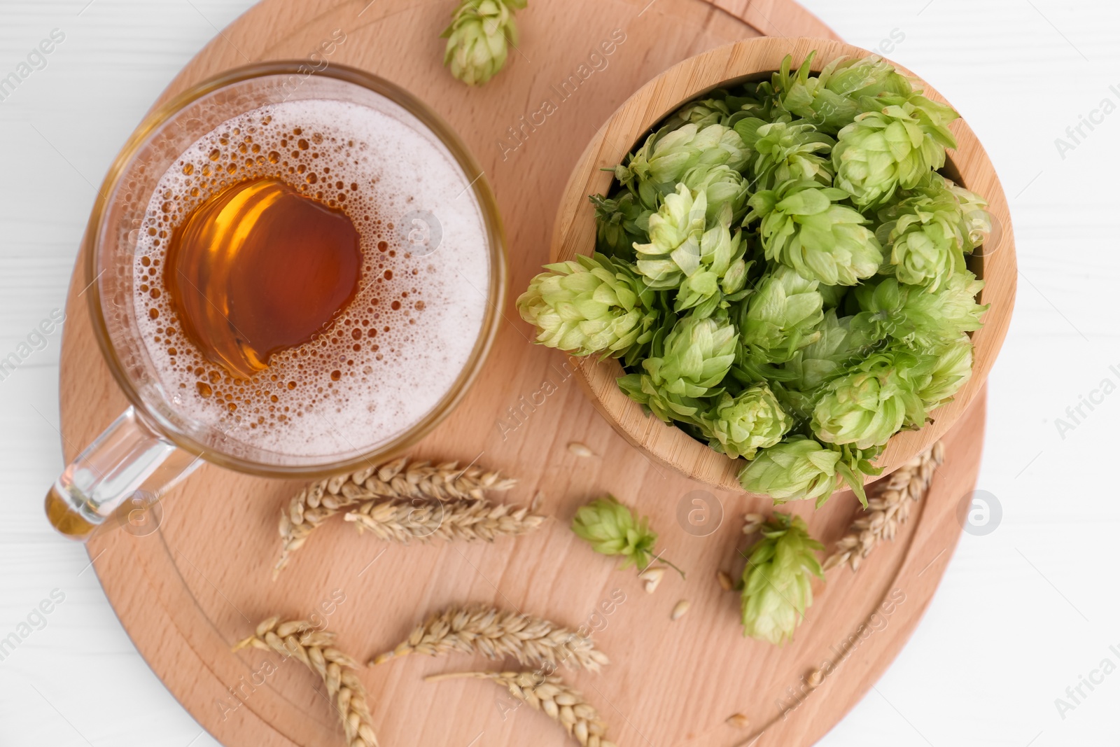 Photo of Mug with beer, fresh hops and ears of wheat on white wooden table, top view