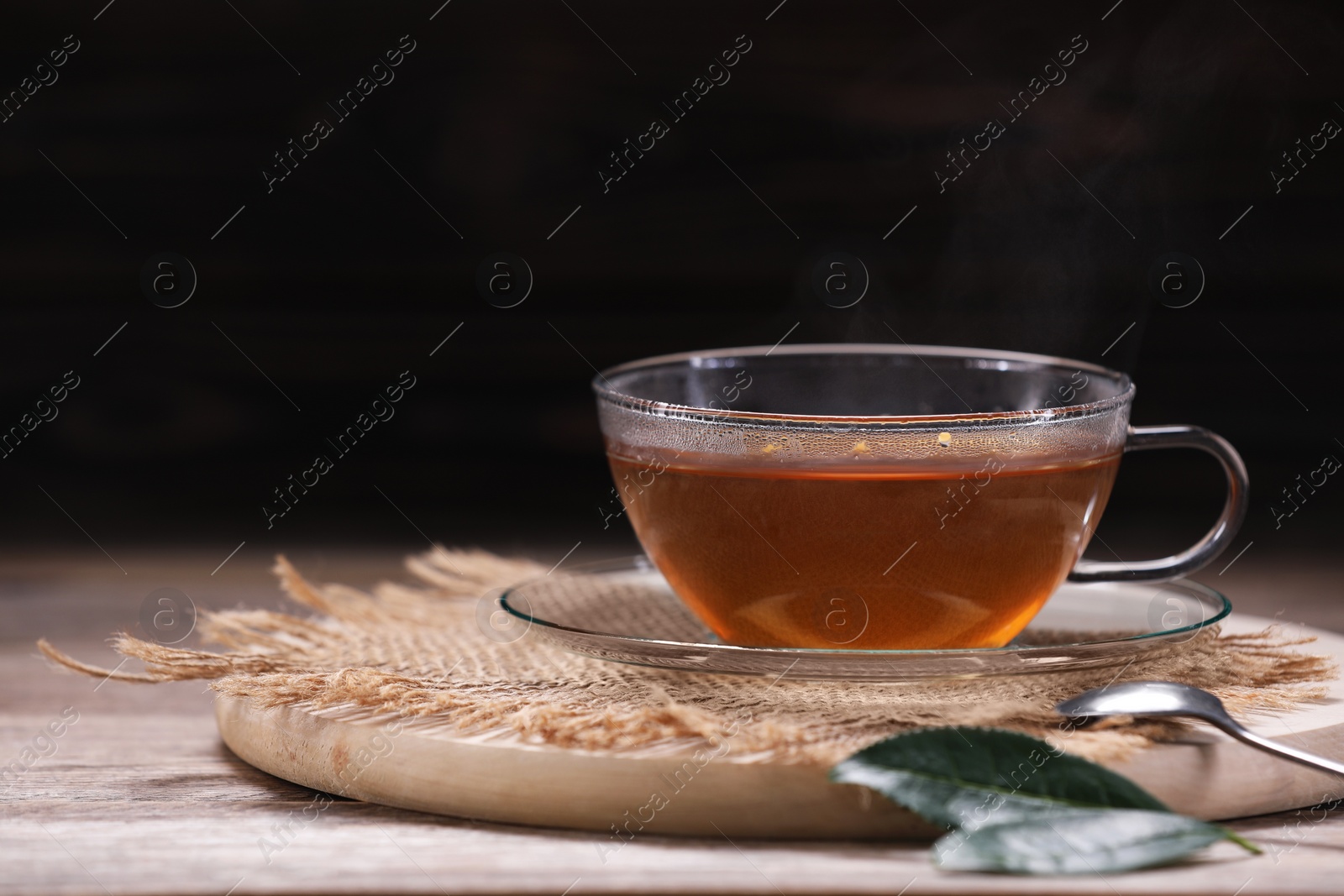 Photo of Aromatic hot tea in glass cup and leaves on wooden table against dark background. Space for text