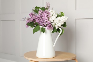 Beautiful lilac flowers in vase on wooden table near white wall