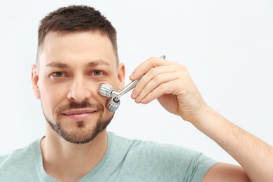Photo of Man using metal facial roller on white background
