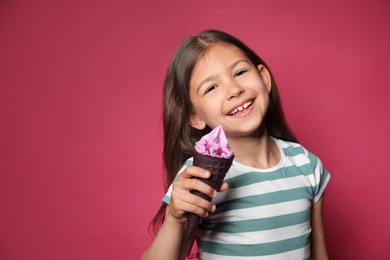 Adorable little girl with delicious ice cream against color background, space for text