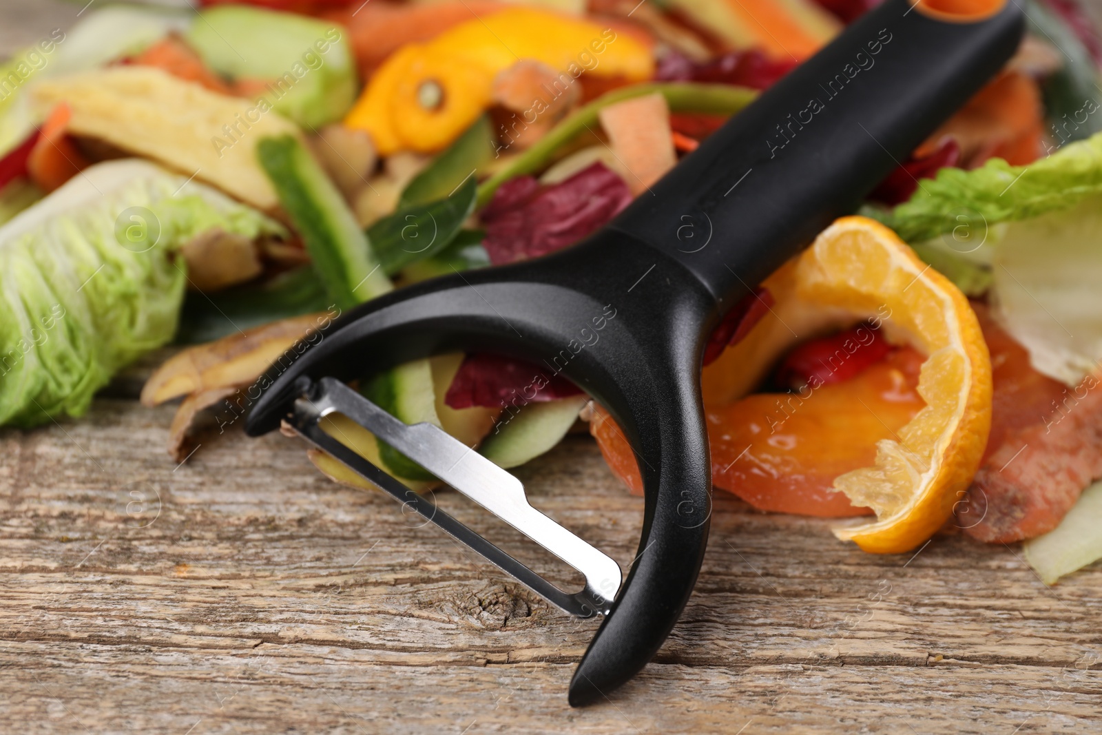 Photo of Peels of fresh vegetables and peeler on wooden table, closeup