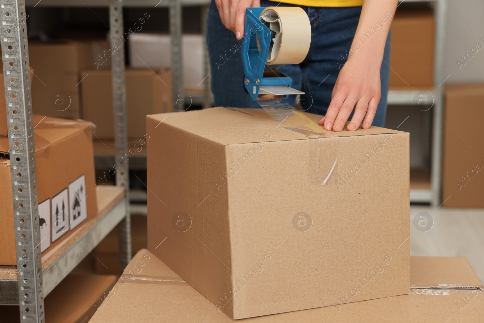 Photo of Post office worker packing box with adhesive tape indoors, closeup