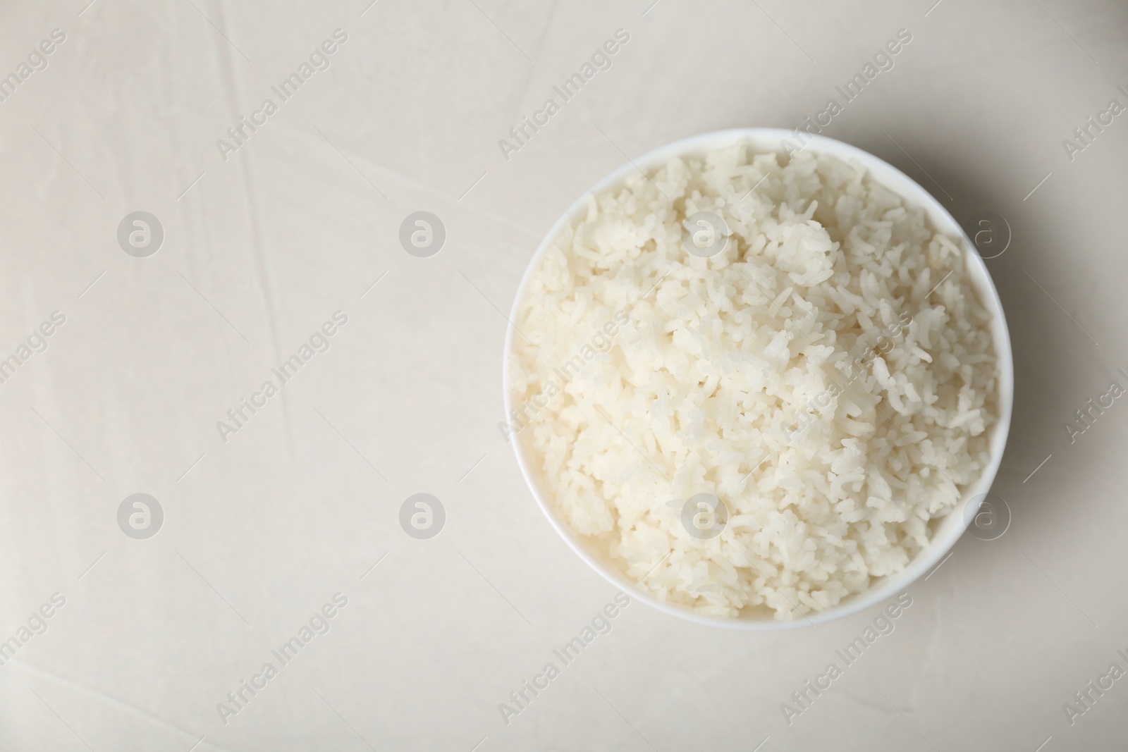 Photo of Bowl of boiled rice on light background, top view with space for text