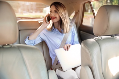 Photo of Young businesswoman with smartphone and laptop in car