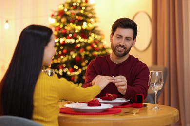 Photo of Making proposal. Man putting engagement ring on his girlfriend's finger at home on Christmas, selective focus