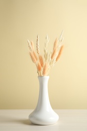 Photo of Dried flowers in vase on table against beige background