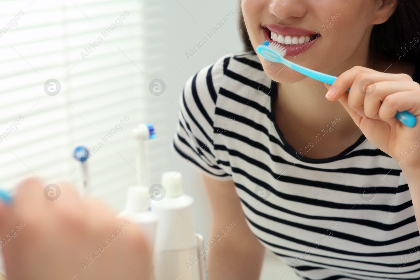 Photo of Woman brushing her teeth with plastic toothbrush near mirror in bathroom, closeup