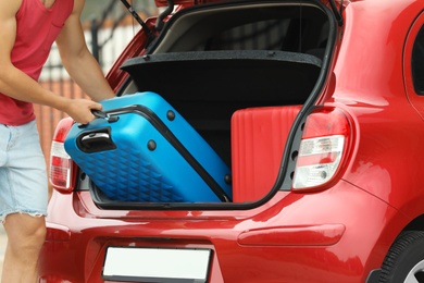 Photo of Man packing suitcase into car trunk outdoors, closeup