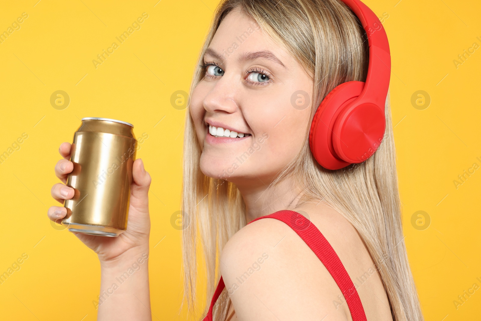 Photo of Beautiful happy woman holding beverage can on yellow background, closeup