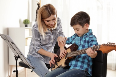 Little boy playing guitar with his teacher at music lesson. Learning notes