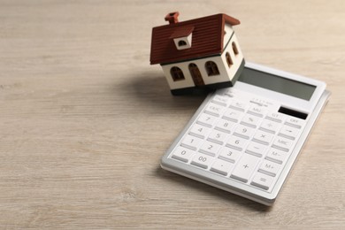Photo of Mortgage concept. House model and calculator on wooden table, closeup with space for text