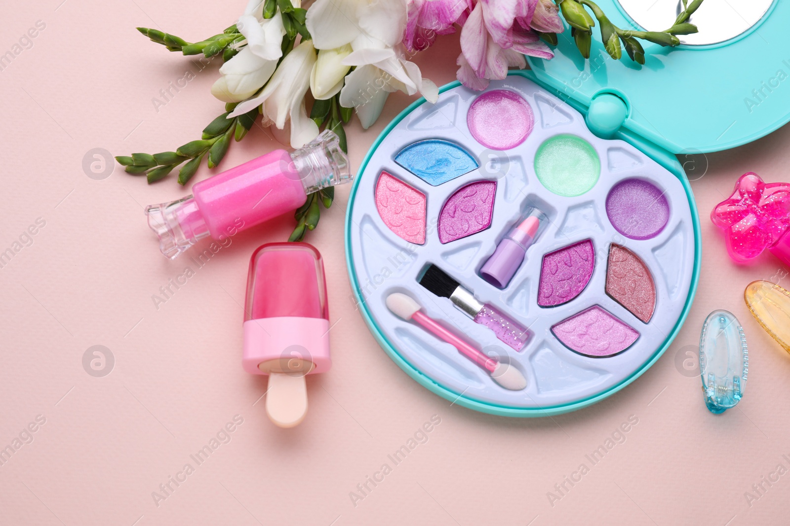 Photo of Decorative cosmetics for kids. Eye shadow palette, lipsticks, accessories and flowers on pink background, flat lay
