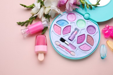 Decorative cosmetics for kids. Eye shadow palette, lipsticks, accessories and flowers on pink background, flat lay