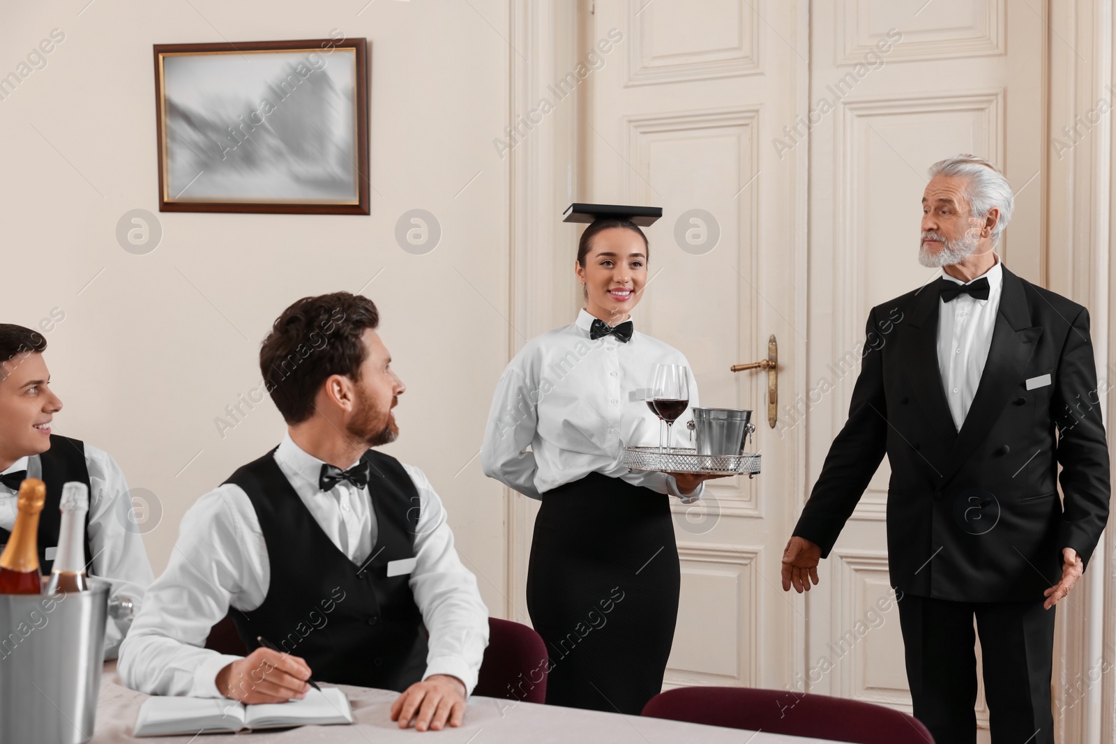 Photo of Senior man wearing formal suit teaching trainees in hotel. Professional butler courses