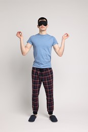 Photo of Man in pyjama and sleep mask meditating on light grey background