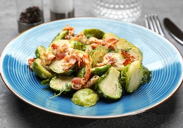 Photo of Delicious cooked Brussels sprouts with bacon served on grey table, closeup