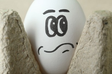 Photo of Egg with drawn thoughtful face in cardboard package, closeup