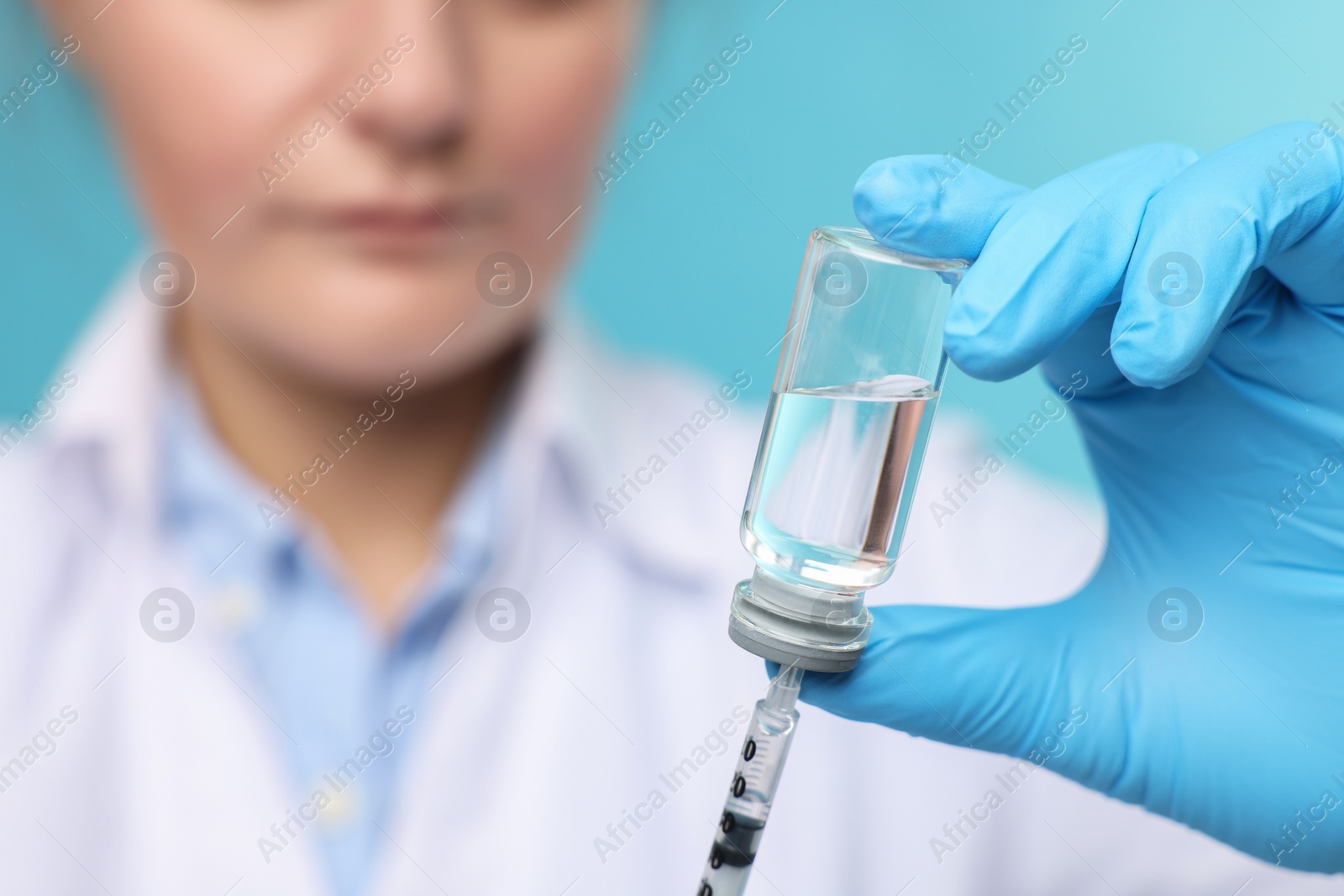 Photo of Doctor filling syringe with medication from glass vial on light blue background, closeup. Space for text