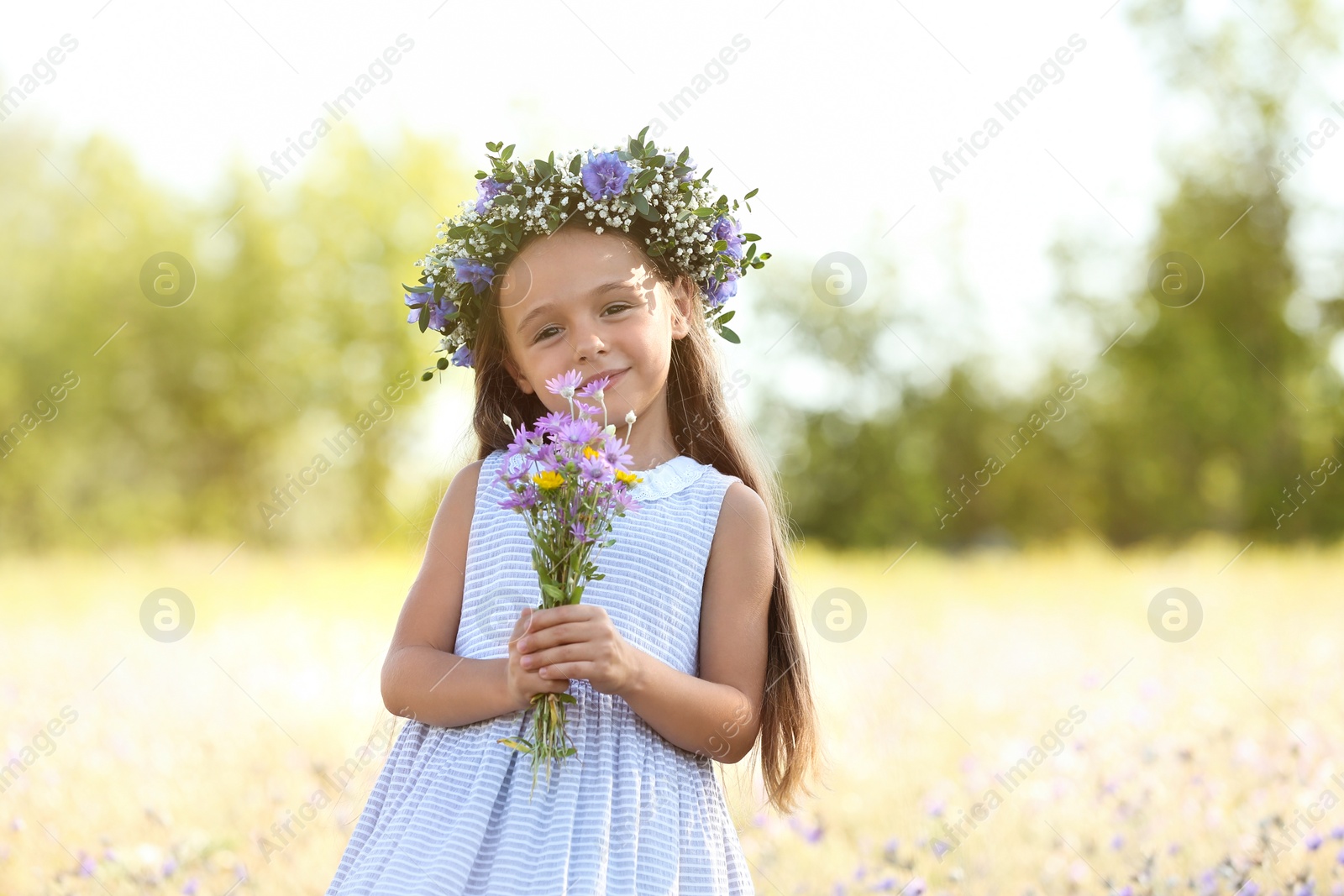 Photo of Cute little girl wearing beautiful wreath with bouquet of wildflowers outdoors. Child spending time in nature