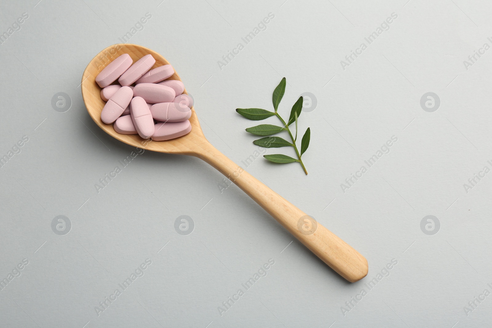 Photo of Vitamin pills in wooden spoon and twig on light grey background, top view. Health supplement