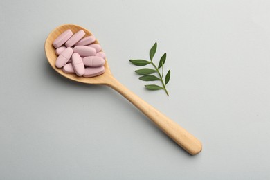 Vitamin pills in wooden spoon and twig on light grey background, top view. Health supplement