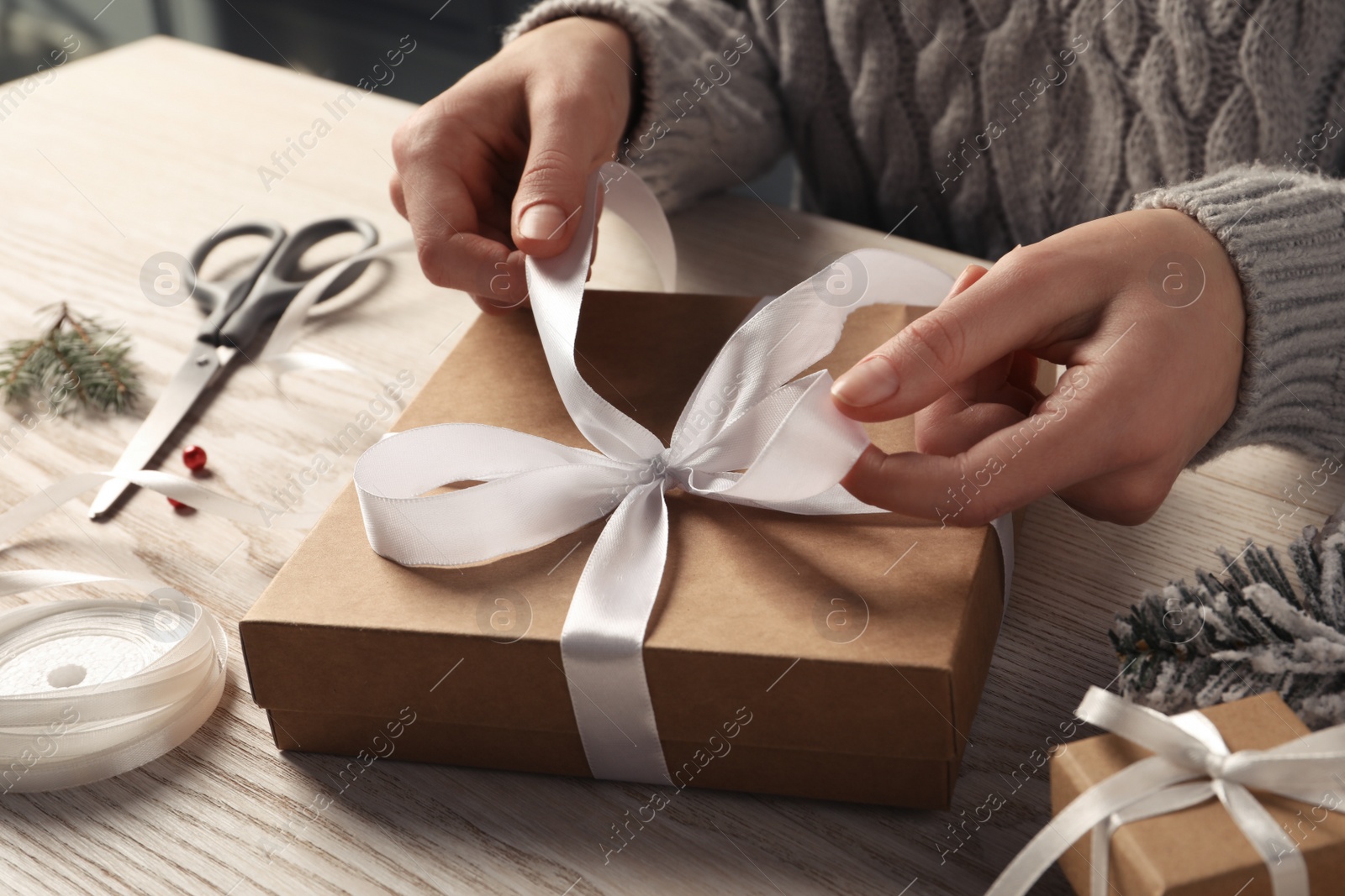 Photo of Woman decorating gift box at white wooden table, closeup. Christmas present