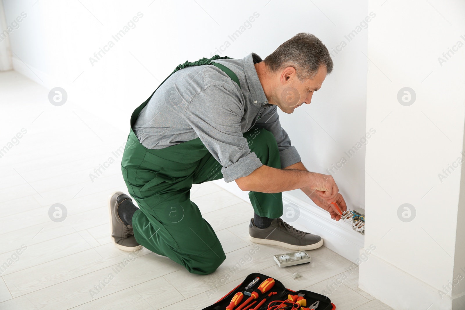 Photo of Electrician with screwdriver repairing power socket indoors