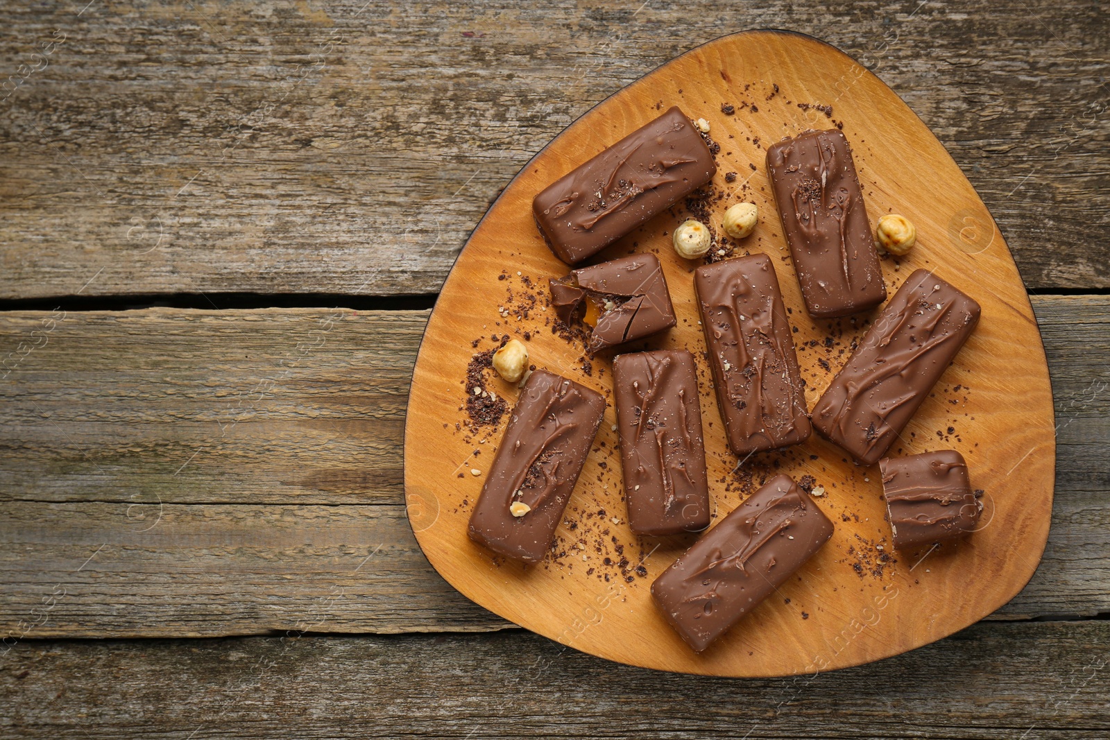 Photo of Delicious chocolate candy bars with nuts on wooden table, top view. Space for text