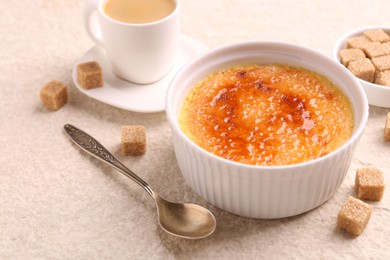 Photo of Delicious creme brulee in bowl, sugar cubes, coffee and spoon on light textured table, closeup