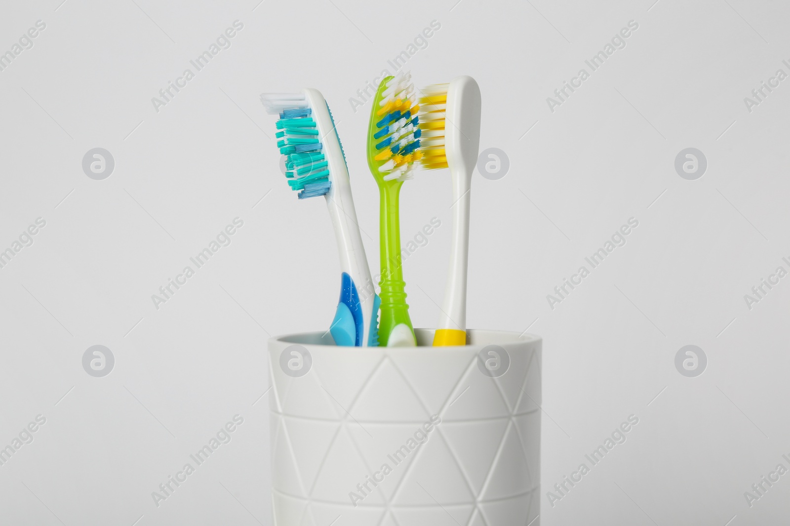 Photo of Different toothbrushes in holder on light grey background, closeup