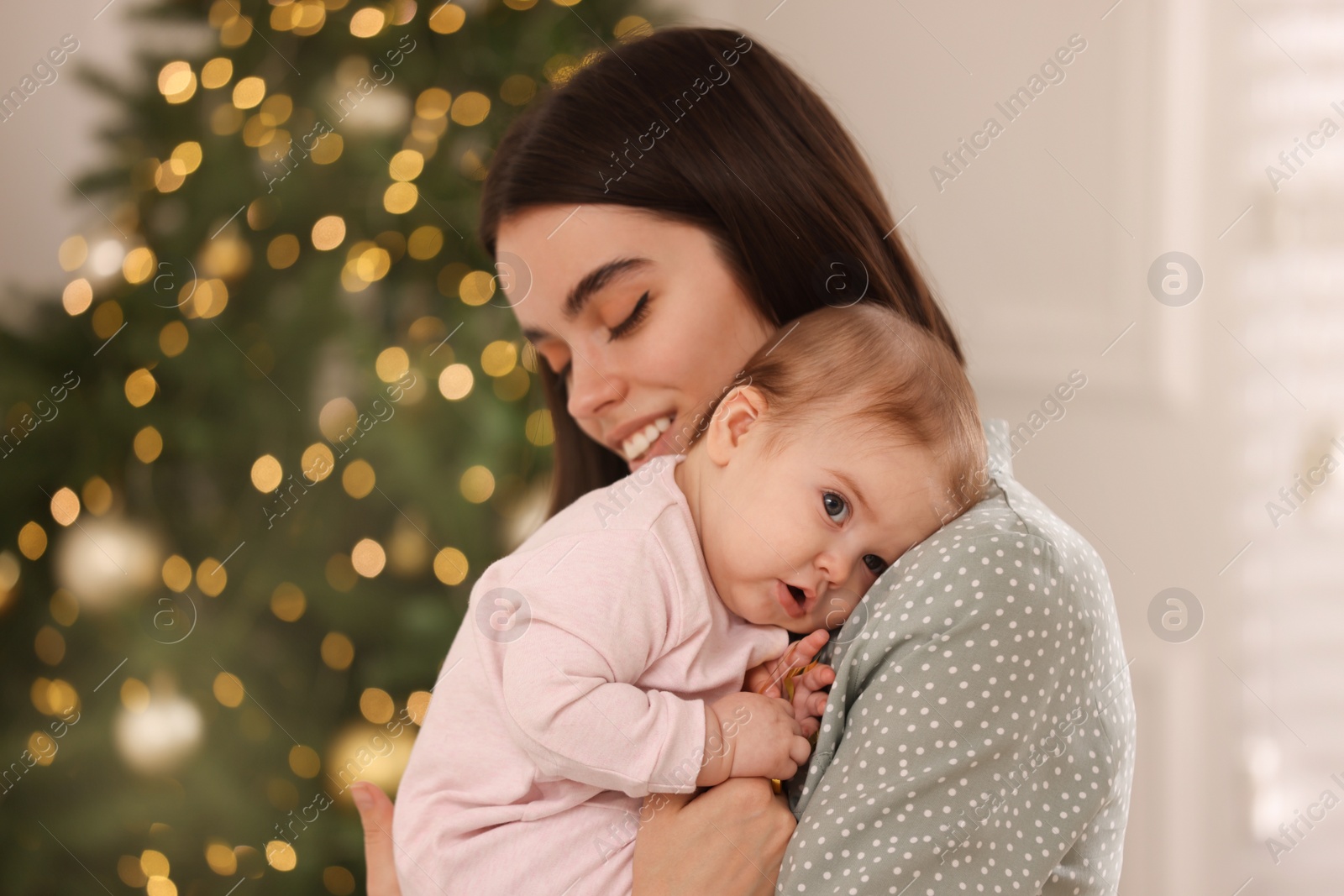 Photo of Happy young mother with her cute baby against blurred festive lights. Winter holiday