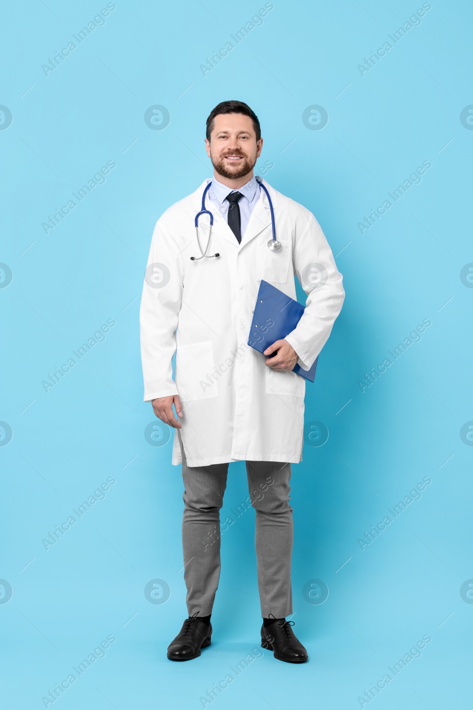 Photo of Smiling doctor with clipboard on light blue background